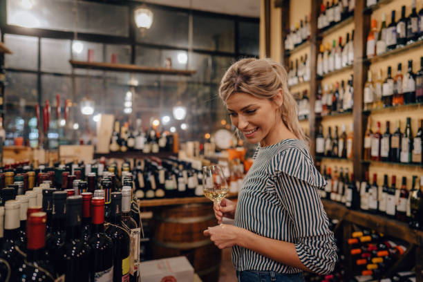 Woman tasting wine in a wine shop Photo of a young woman drinking wine in a local wine shop; trying different types of wine and enjoying her first wine tasting experience. alcohol shop stock pictures, royalty-free photos & images