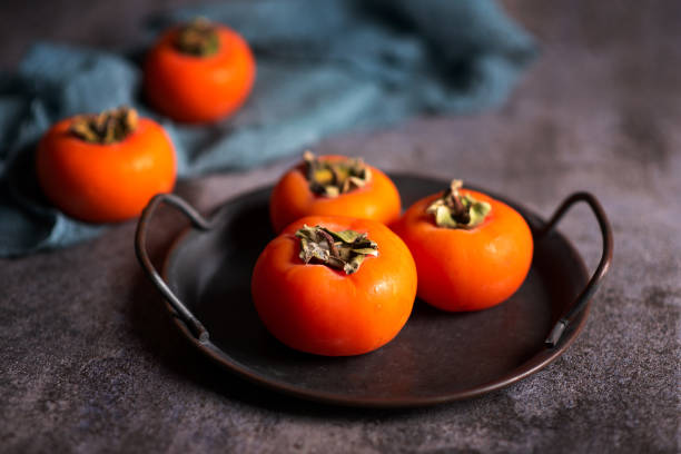 плоды хурмы оранжевого каки на деревенской тарелке - persimmon стоковые фото и изображения