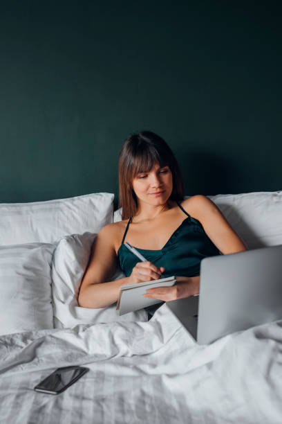 istock Attractive Young Woman in Lingerie Taking Notes and Using a Laptop while Lying in Bed 1288157123