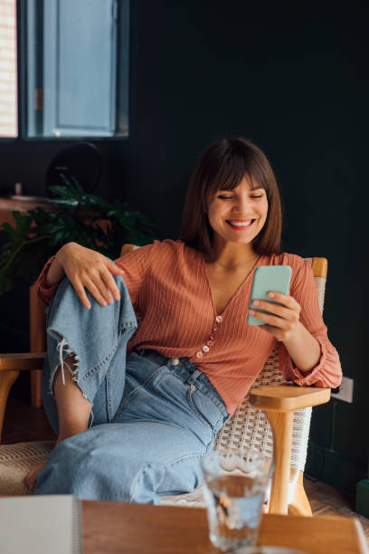 istock Beautiful Cheerful Young Woman Using a Mobile Phone while Sitting Casually in a Chair 1288157138
