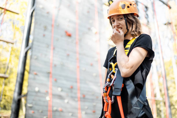 Female climber securing ropes on rocky mountain face wearing helmet and harness. Woman engaged in outdoor rock climbing adventure with safety equipment. Active person climbing rocks in nature.