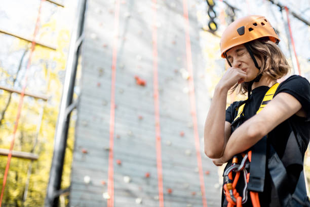 Low angle view of a woman wearing safety equipment and harness training on the artificial climbing wall. Female professional rock climber hanging with rope and looking down while practicing at training center.