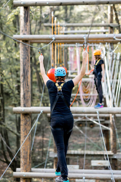 Well-equipped man and woman having an active recreation, climbing ropes in the park with obstacles outdoors