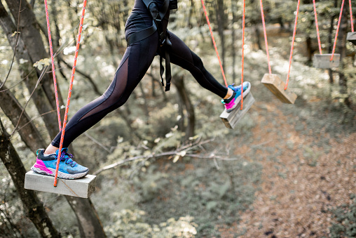 Young well-equipped woman having an active recreation, climbing ropes in the park with obstacles outdoors, close-up on legs