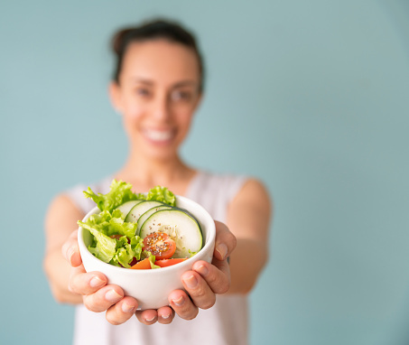 Healthy eating woman holding a salad and showing it to the camera - focus on foreground