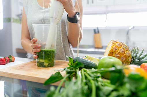 Close-up on a woman making a healthy green smoothie with an immersion blender