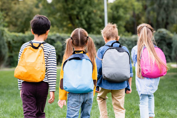 istock Back view of schoolkids with backpacks walking on lawn 1288162708