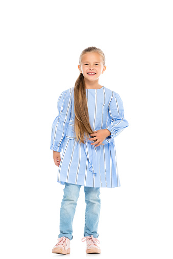 Cheerful girl in dress and jeans looking at camera on white background