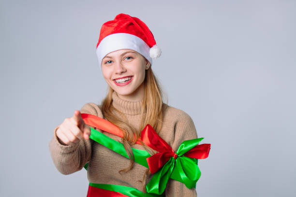 istock Happy blonde in a Santa hat laughs and points a finger at the camera. White background with empty space. 1288163634