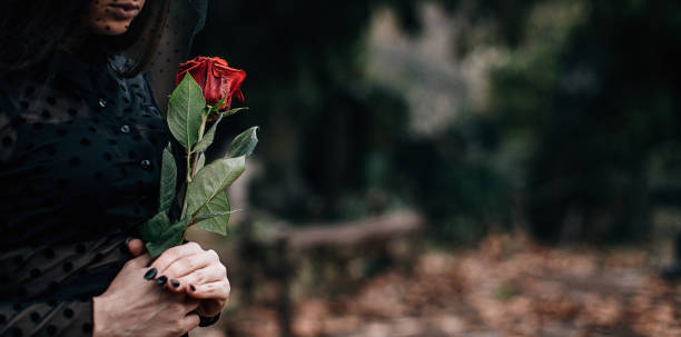 istock One sad widow grieves in a cemetery holding rose 1288164499
