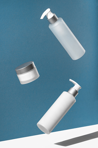 Jar and bottles for cosmetics in the air on a blue background. levitation. Body care creative concept.