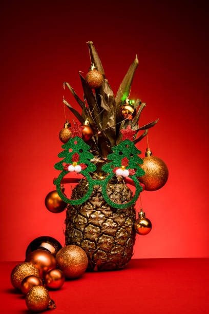 istock Golden pineapple decorated with Christmas sunglasses on red background. 1288168527