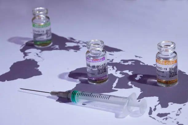 Distribution of a vaccine. World map with COVID-19 (SARS-CoV-2) corona vaccine vials and injection syringe.

Notes:
- QR code on bottles was generated by my and contains generic text: "SARS-CoV-2 Vaccine""
- World map is in Public Domain: see: https://commons.wikimedia.org/wiki/File:BlankMap-World-noborders.png (author  E Pluribus Anthony has put it in public domain: see article in previous link)