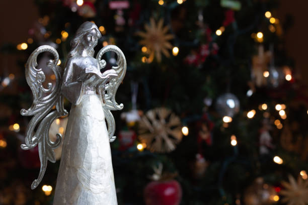 Silver Angel Statue reading book in front of Christmas tree with lights with copy space