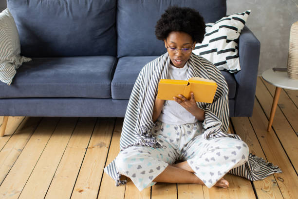 Happy African American young woman sit relax on cozy couch and reads a book. Happy to move to new apartment. stock photo