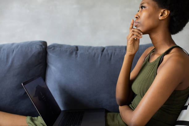 Happy african American young woman sit relax on cozy couch and working on a laptop. Happy to move to new apartment stock photo