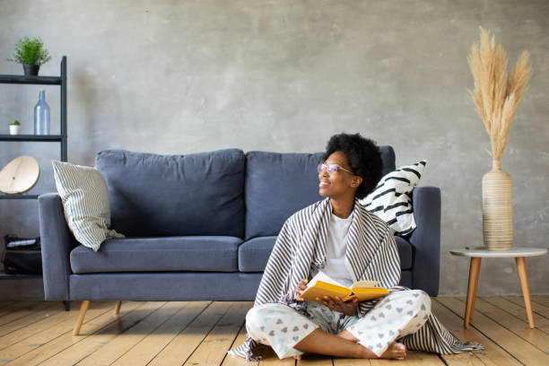 Happy African American young woman sit relax on cozy couch and reads a book. Happy to move to new apartment. stock photo