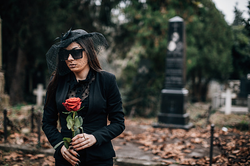One young sad woman, widow, visiting a loved one at the cemetery. Paying respect with fresh rose flower.