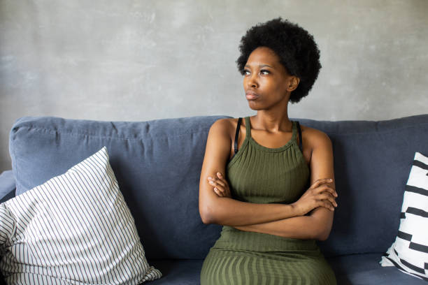 Unhappy African American woman sit on the sofa, the girl is very upset sitting on the couch of her apartment. stock photo