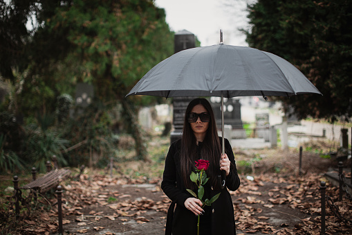 One young sad woman, widow, visiting a loved one at the cemetery. Paying respect with fresh rose flower.