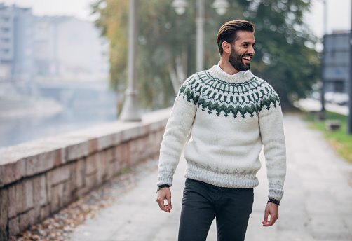 One young handsome man dressed in modern winter sweater standing outdoors in the city.