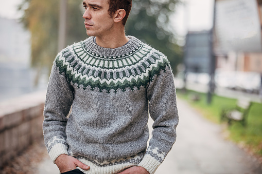 One young handsome man dressed in modern winter sweater walking outdoors in the city.