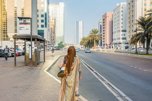 An Arabic woman wearing traditional clothes and hijab waiting for bus at the bus station of Abu Dahbi, United Arab Emirates.