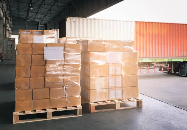 istock Cargo shipment boxes, Freight truck, Warehousing. Stacked of package boxes wrapping plastic on pallet waiting to load into shipping container. Logistics and transportation. 1288194493