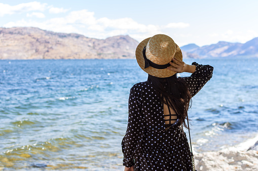 Young woman wearing a straw hat gazing out onto Okanagan Lake in British Columbia, Canada. Optimistic, hopeful, youthful and holiday concept. Image can be utilized editorially or commercially.