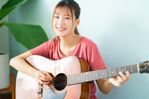 Young Asian girl is learning to play the guitar at home