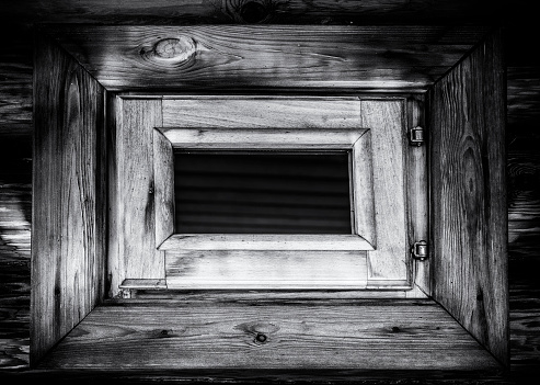 A small window in an old wooden log house. Black and white photo.