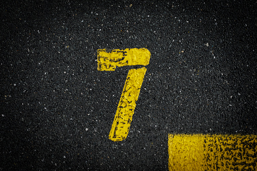 sign on the asphalt, yellow painted number seven on grey street, yellow lines like a corner on the road, space for text