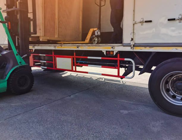 istock Worker driving forklift loading shipment carton boxes goods on wooden pallet at loading dock from container truck to warehouse cargo storage in freight logistics, transportation industrial, delivery 1288207536