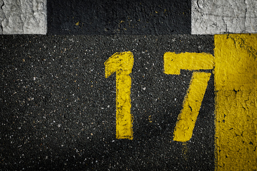 sign on the asphalt, yellow painted number seventeen on grey street, yellow lines like a corner on the road, space for text