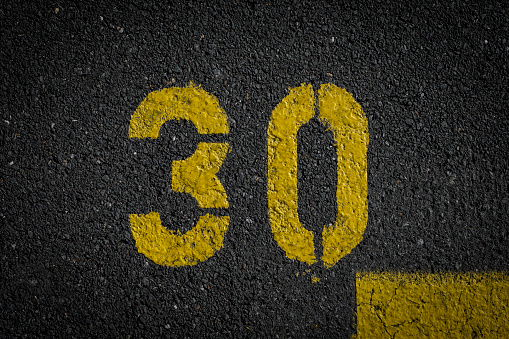 sign on the asphalt, yellow painted number thirty on grey street, yellow lines like a corner on the road, space for text