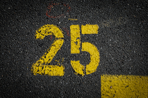 sign on the asphalt, yellow painted number twenty five on grey street, yellow lines like a corner on the road, space for text