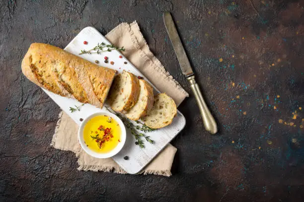 Top view of fresh wholegrain bread with olive oil, old table-knife and thyme spice on dark grunge background