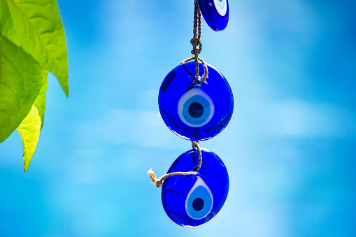 Close up shot of hanging traditional blue evil eyes amulet,made by glass, in a blue bokeh background