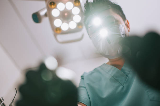 asiático chino hombre dentista endodoncista con gafas de aumento y luz mirando desde arriba al paciente - dental drill fotografías e imágenes de stock