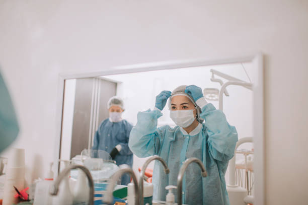 asiática china mujer dentista usando ropa de trabajo protectora ppe frente al espejo en la oficina del dentista conseguir cirugía lista - hair net nurse scrubs asian ethnicity fotografías e imágenes de stock