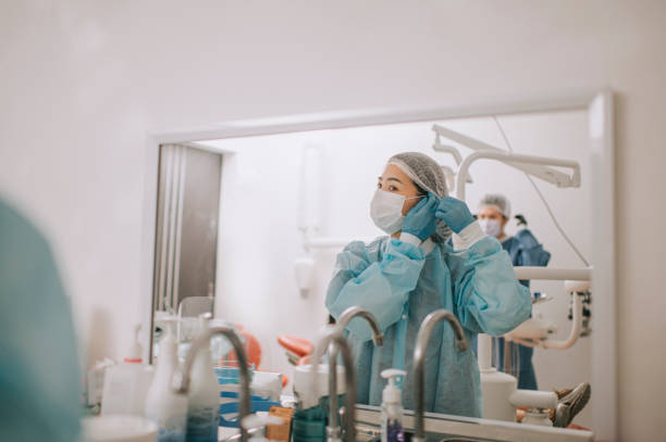 asiática china mujer dentista usando ropa de trabajo protectora ppe frente al espejo en la oficina del dentista conseguir cirugía lista - hair net nurse scrubs asian ethnicity fotografías e imágenes de stock