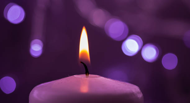 istock Close up of one burning candle with blurred Christmas light background 1288231499