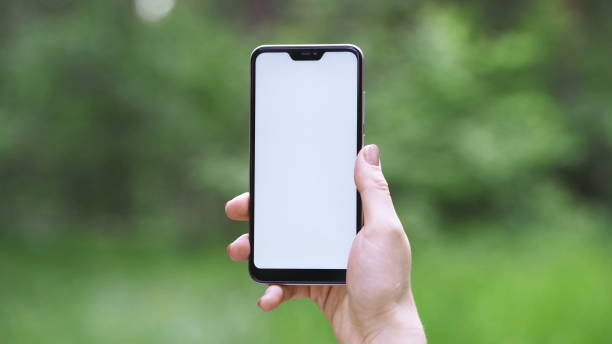 istock Female hand holding vertical black smartphone with green screen chroma key for tracking motion on the blurred city street background in sunny day. 1288232735