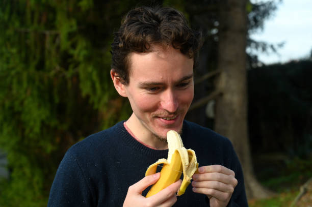 istock Young man peeling a banana and eating it 1288233630