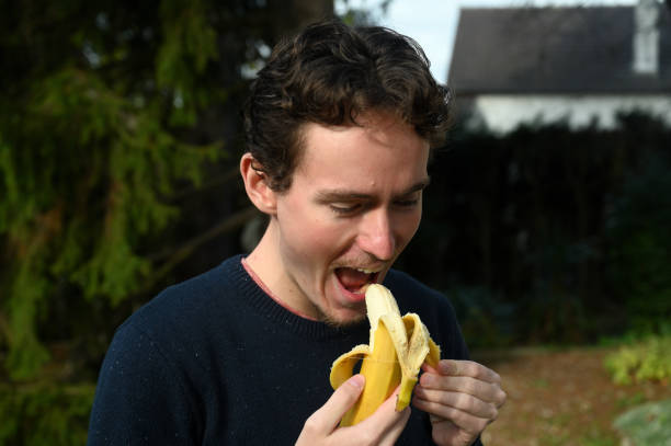 istock Young man peeling a banana and eating it 1288233664