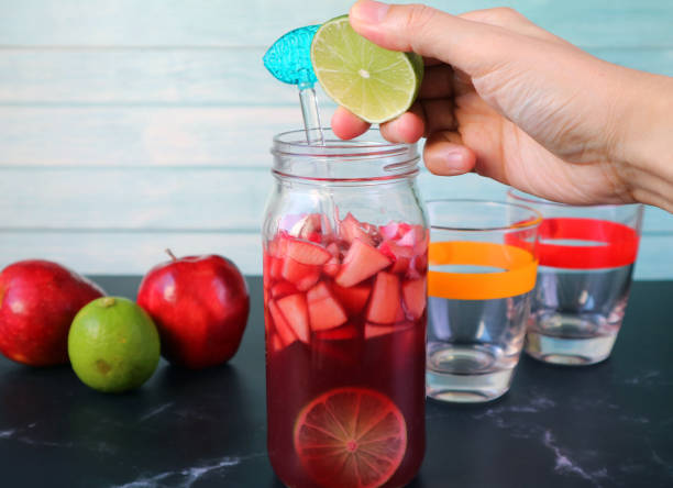 Man's Hand Squeezing a Slice of Lime into the Bottle of Red Wine Sangria