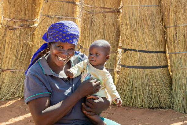 femme africain s’asseyant dans la cour de son village - africa child village smiling photos et images de collection