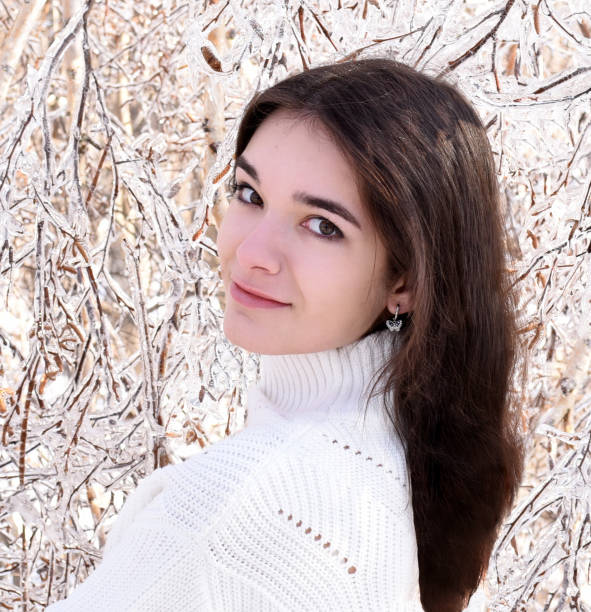 ritratto di giovane donna russa in maglione bianco che guarda la macchina fotografica accanto a rami ghiacciati di betulle, ricoperti di ghiaccio. foresta invernale in russia - russian ethnicity cold relaxation nature foto e immagini stock
