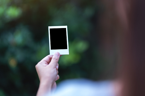 A woman holding mockup of polaroid photo frame with blurred background