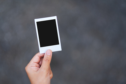A hand holding mockup of polaroid photo frame with blurred background